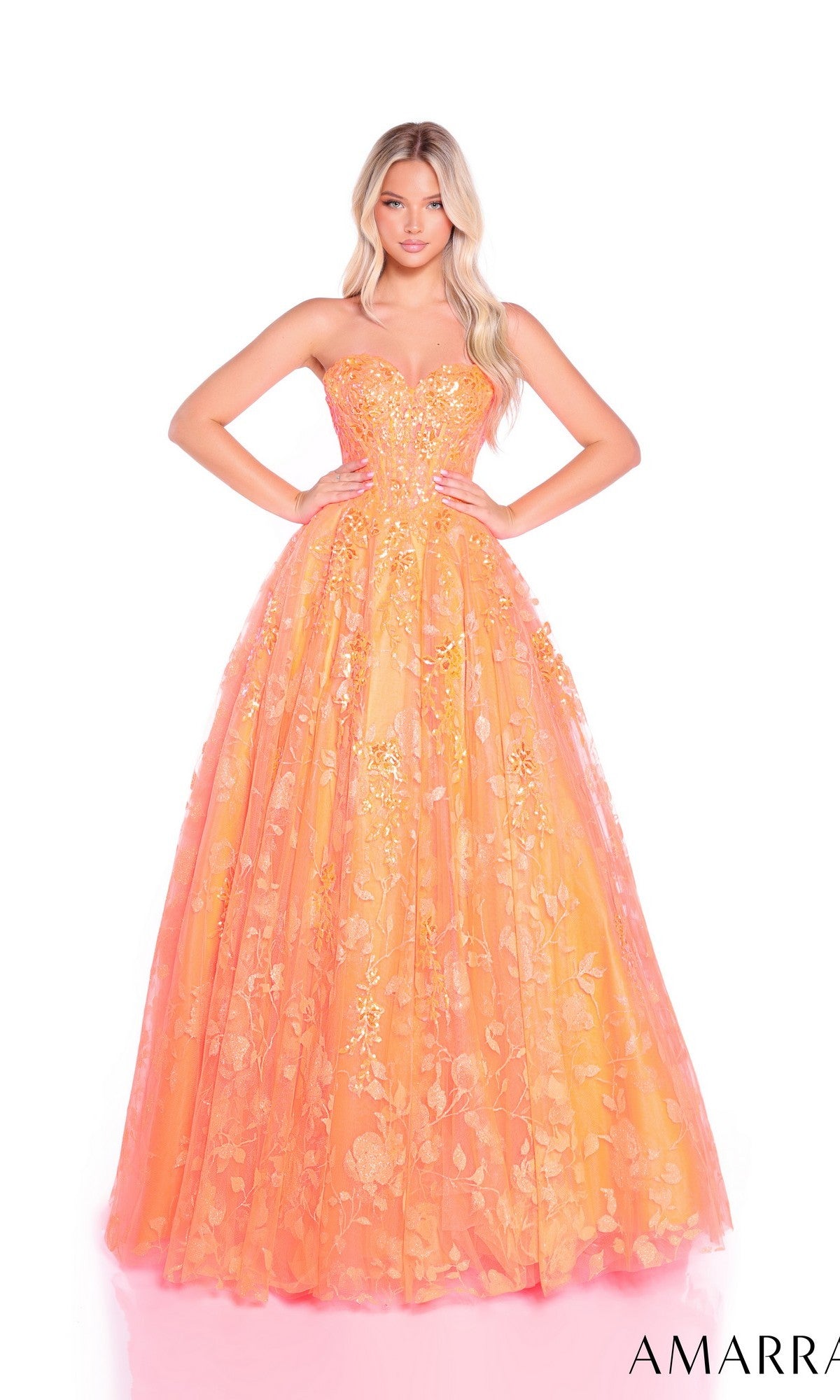 A woman stands with hands on hips against a white background, wearing the Amarra 89513 long prom dress featuring a strapless lace-embroidered corset and floor-length orange and pink floral-embroidered tulle.